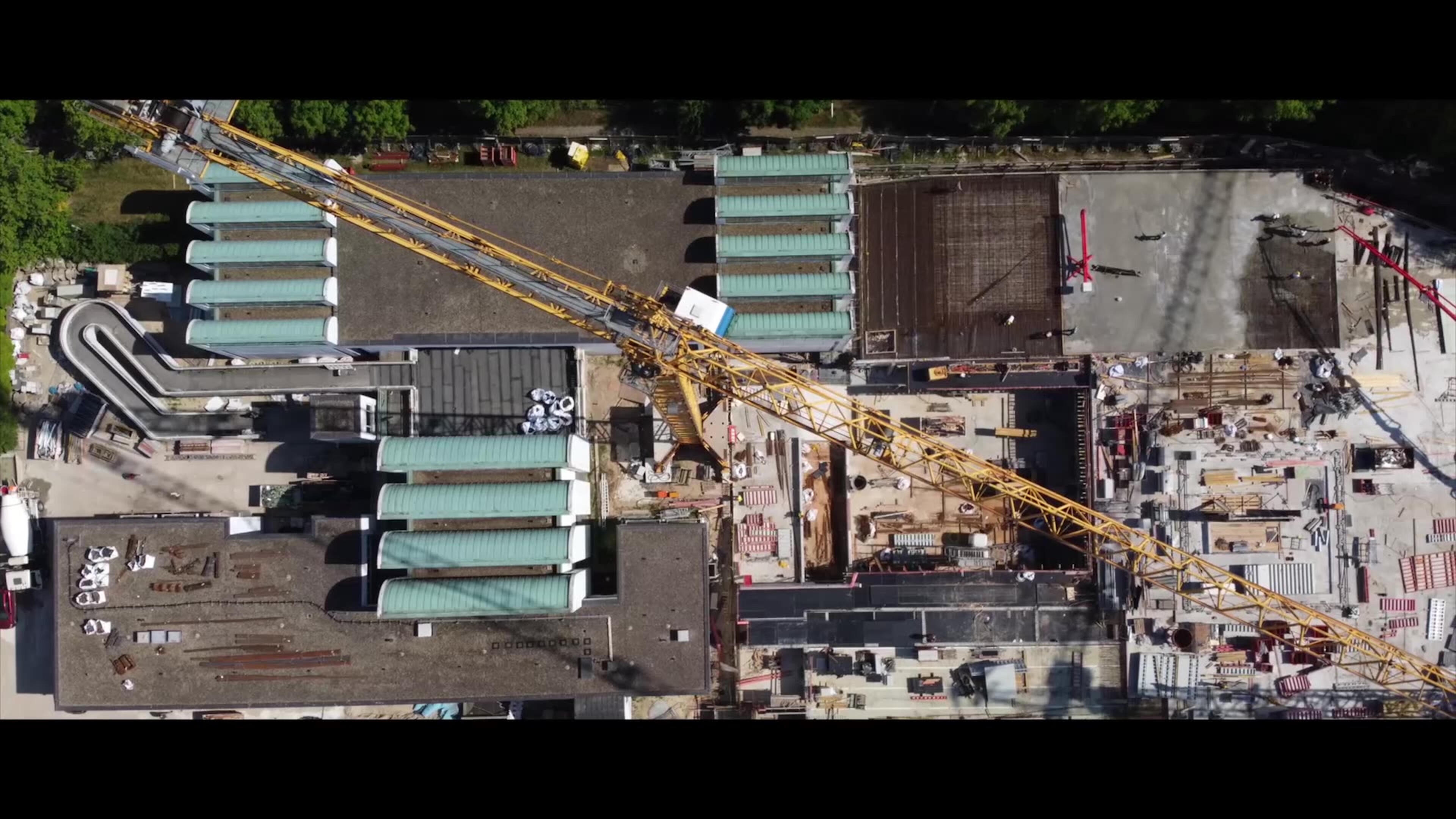 Construction site, aerial view — the ongoing rebuilding as the film’s central condition.